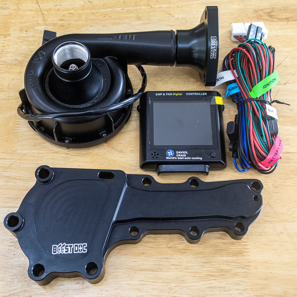 An electric water pump kit including a black mechanical water pump, a control box, wiring, and mounting components laid out on a wooden surface RB25, RB26, RB30 Electric Water Pump (EWP) Kit – Optimal Cooling