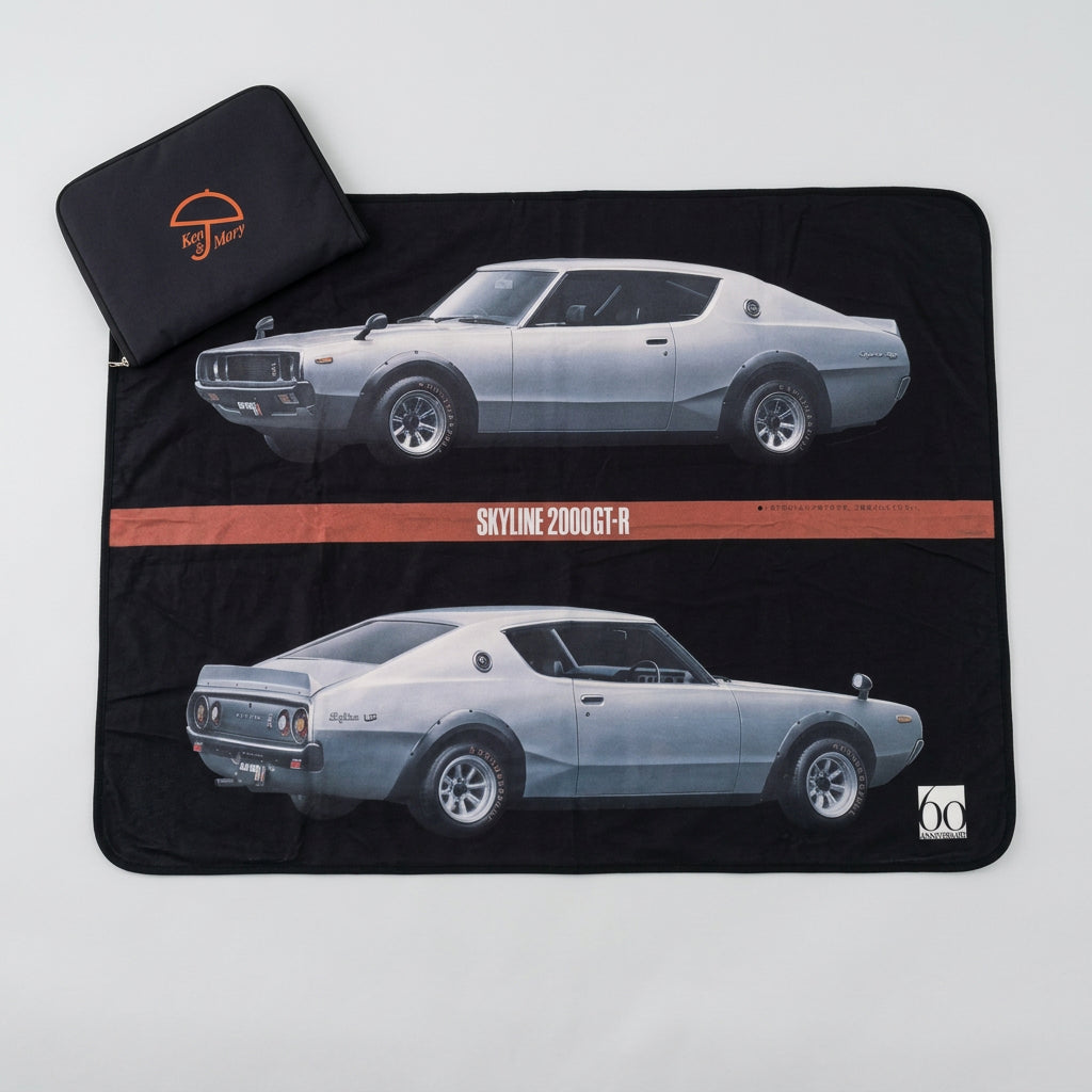 A black picnic blanket with a limited edition print of the Ken & Mary Skyline 2000GT-R car, displayed on a floor mat with a small carry case Ken & Mary Skyline 2000GT-R  Towel