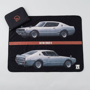 A black picnic blanket with a limited edition print of the Ken & Mary Skyline 2000GT-R car, displayed on a floor mat with a small carry case Ken & Mary Skyline 2000GT-R  Towel