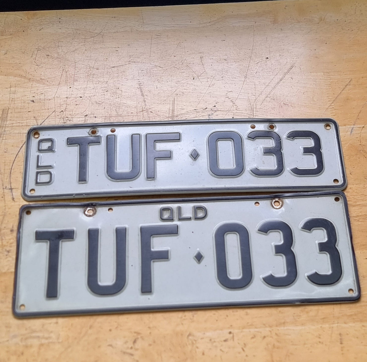 Two Queensland personalized number plates with the text 'TUF 033' on a wooden surface
