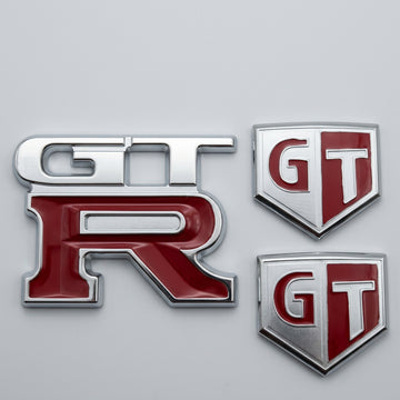 A set of custom OE-styled billet badges with anodised silver finish and red enamel accents, including 'GT' and 'GTR' emblems.