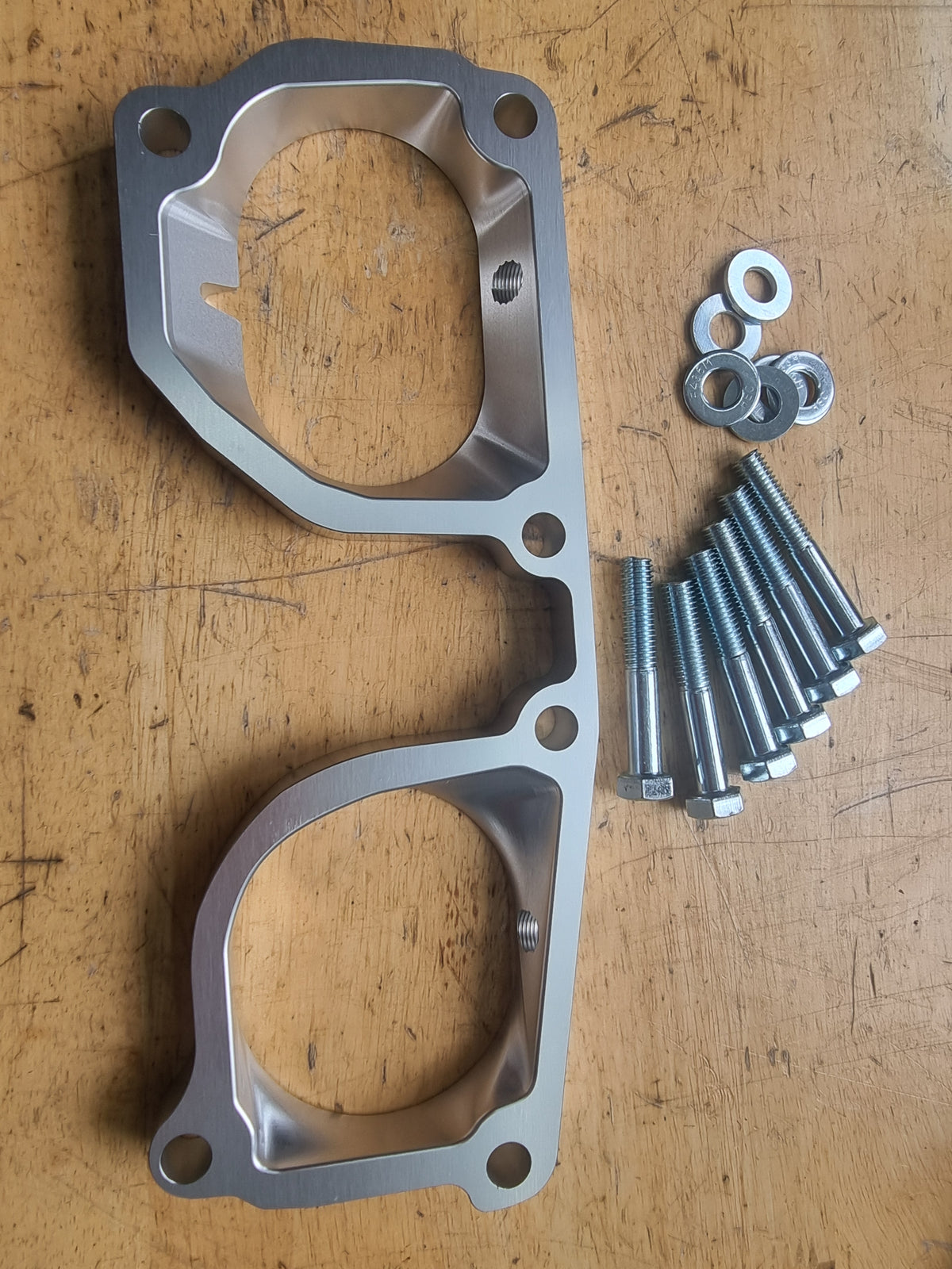 A TB48 Patrol Plenum Spacer made of metal, with an anodized silver finish, displayed alongside an assortment of mounting screws and bolts