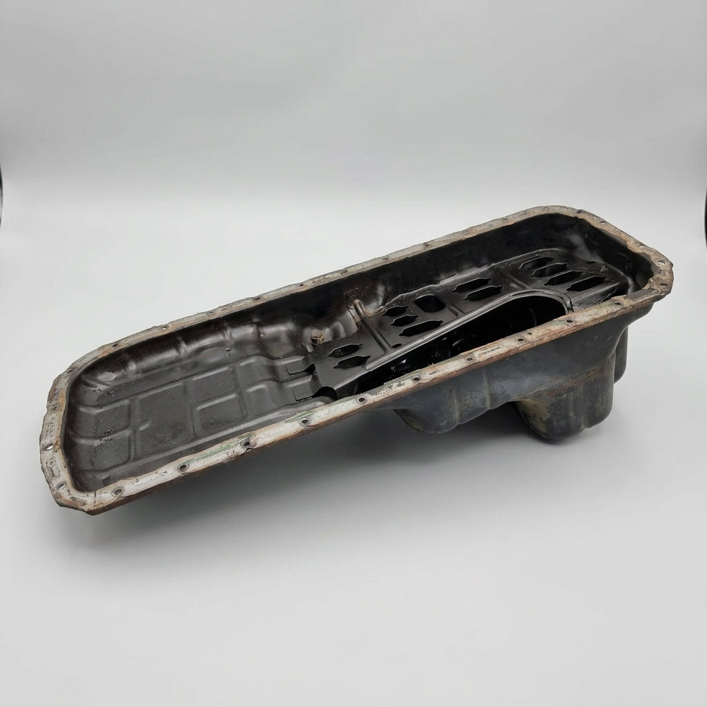 A black deep rear hump oil pan, presumably made of metal, with visible signs of wear and dirt Used RB Deep Rear Hump Oil Pan skyline replacement parts genuine oem nissan part