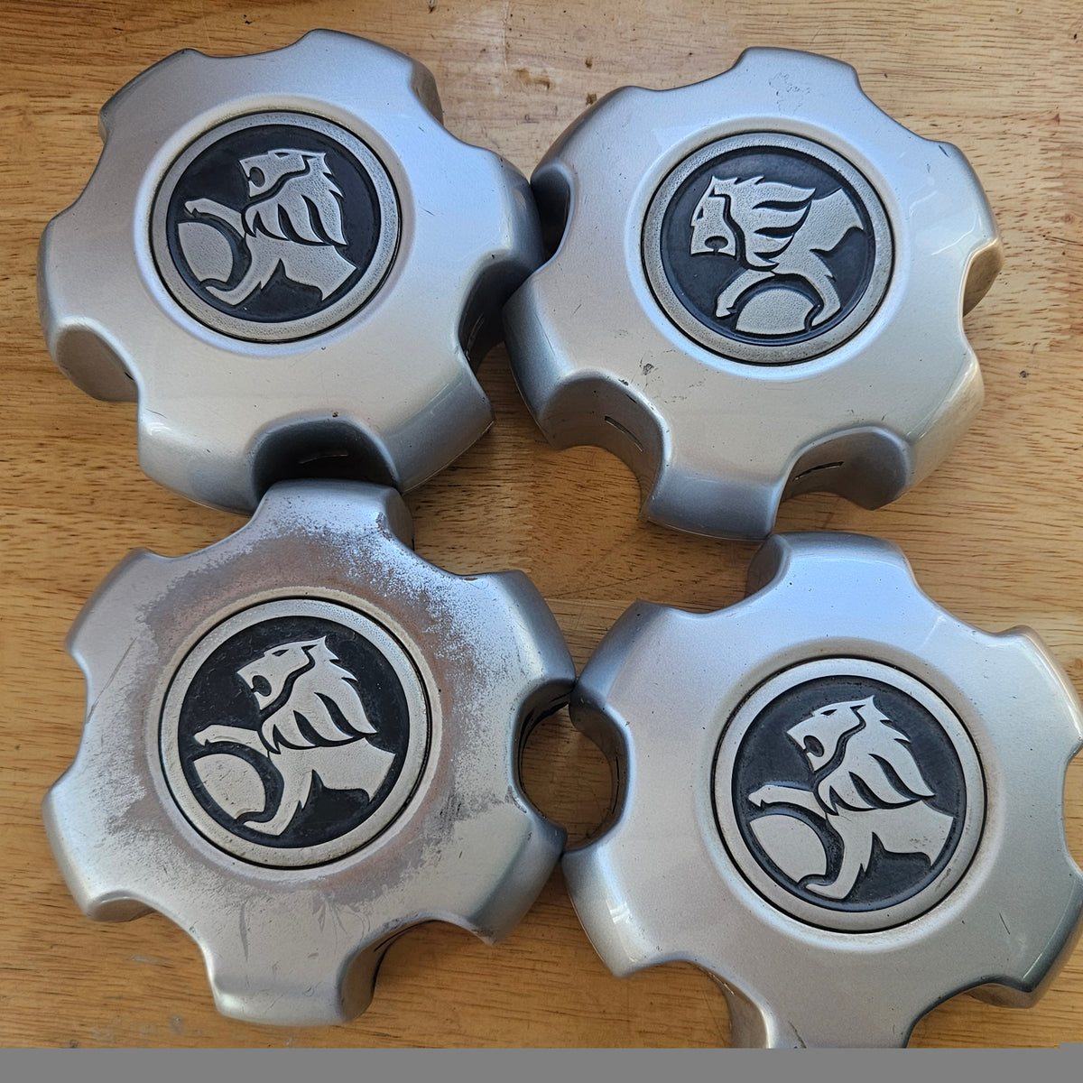 Four silver metal wheel hub covers with the Skoda lion logo in the center, arranged on a wooden surface.